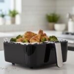 Air fryer basket with aluminum foil cooking seasoned chicken drumsticks and broccoli in a modern kitchen